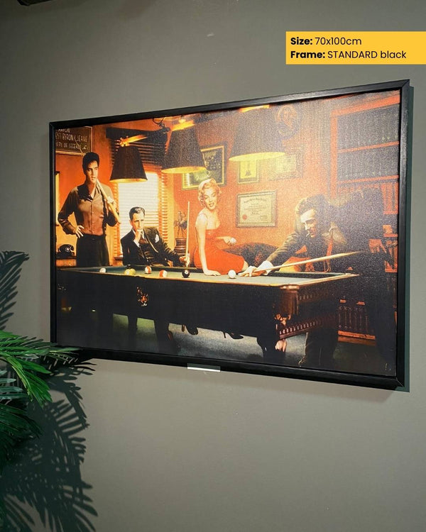 Framed artwork of a pool table scene on a wall with a plant to the left.