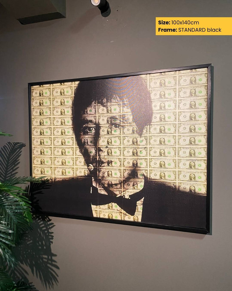 Framed artwork of a face with dollar bill pattern on a gray wall.