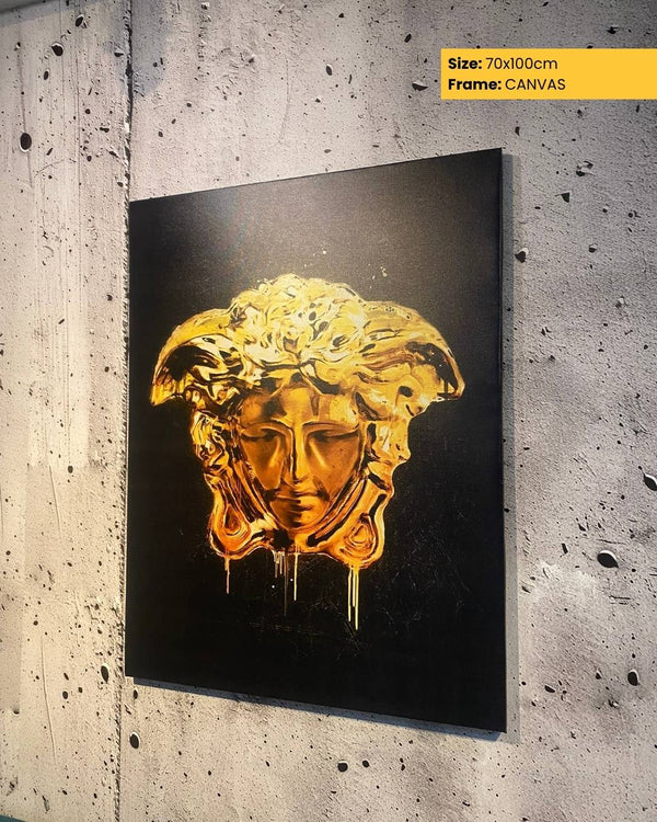 Gold mask artwork on a black background, framed as canvas, against a textured wall.