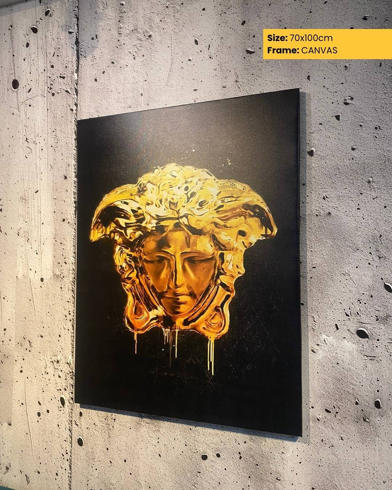 Gold mask artwork on a black background, framed as canvas, against a textured wall.