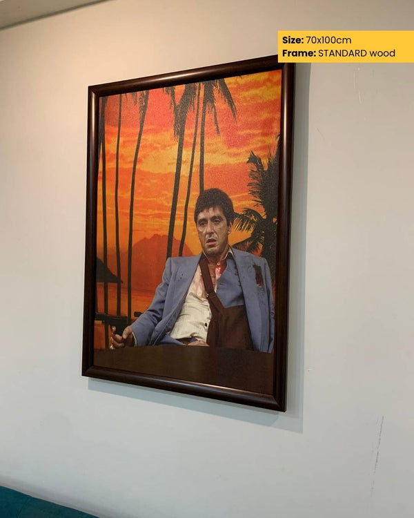 Framed artwork of a person in a blue jacket against a sunset palm tree background on a white wall.