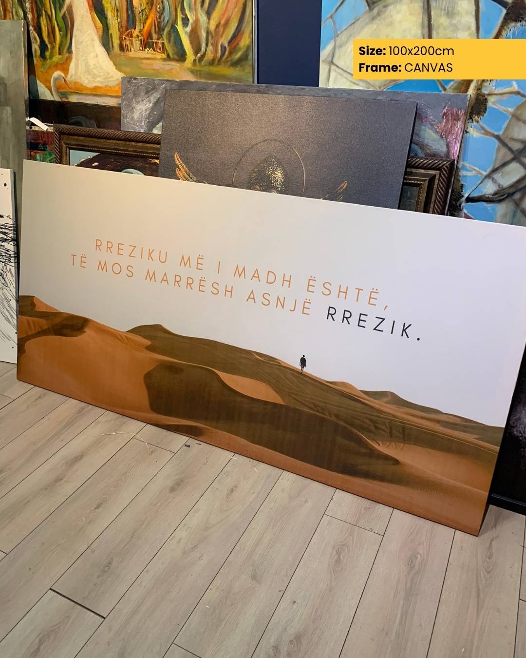 Canvas print with desert landscape and text on a wooden floor, surrounded by other artworks.