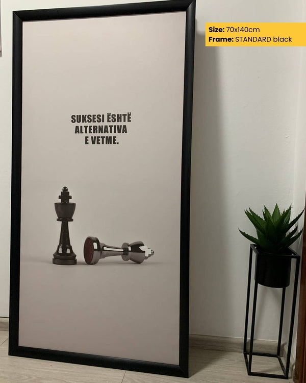 Framed poster with chess pieces and text on a light background, next to a plant.