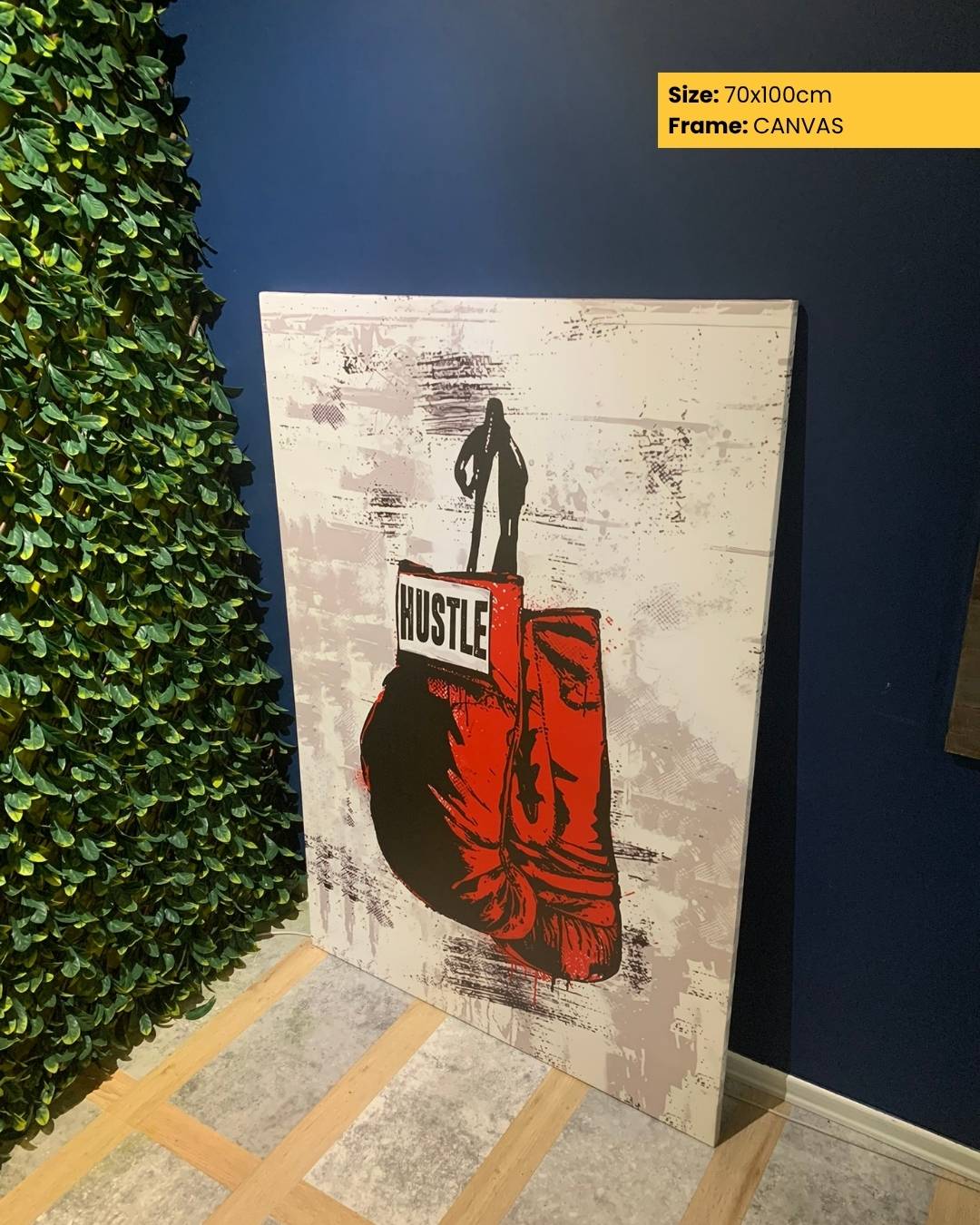 Canvas print with a graphic design of a person holding boxing gloves and the word 'HUSTLE' on a textured background, leaning against a wall.