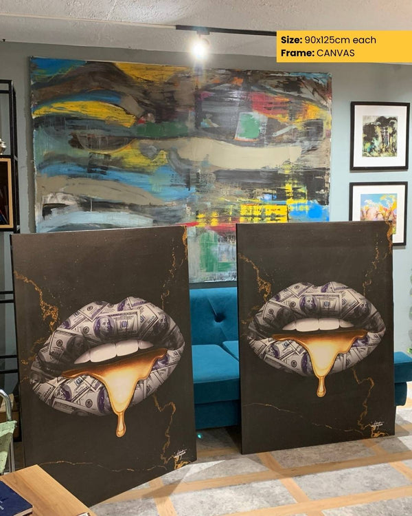Two abstract art pieces on a table with a colorful painting in the background.