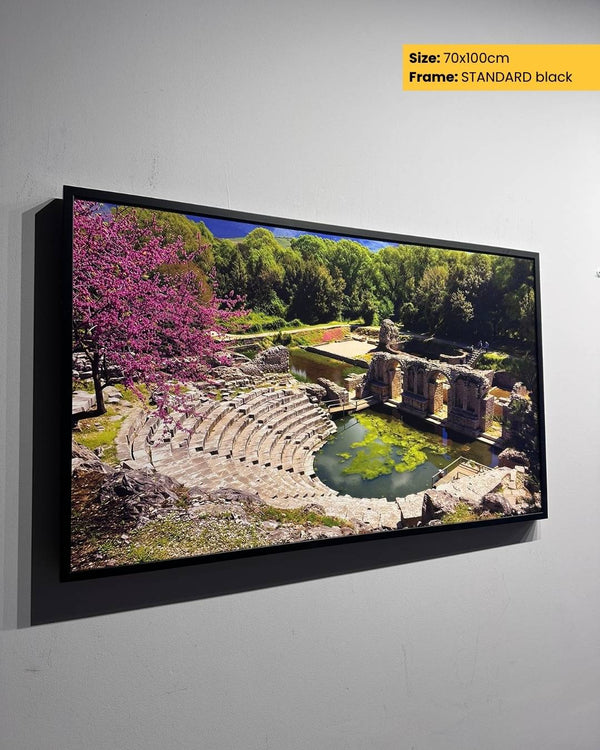 Framed artwork of an outdoor scene with ruins and trees on a gray wall.