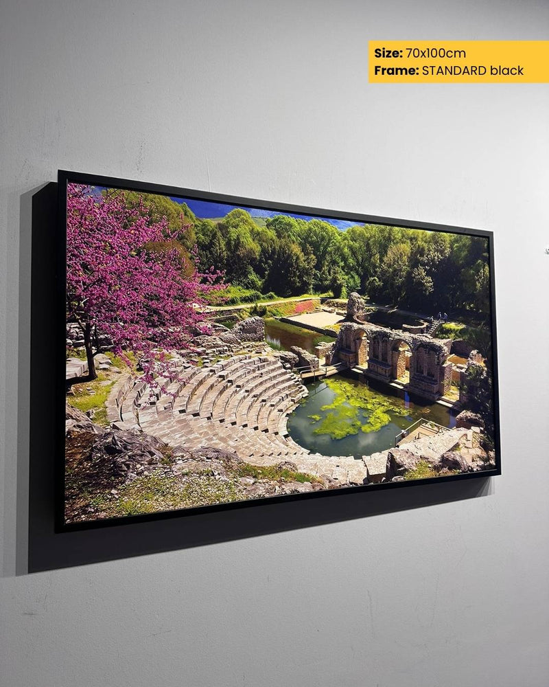 Framed artwork of an outdoor scene with ruins and trees on a gray wall.