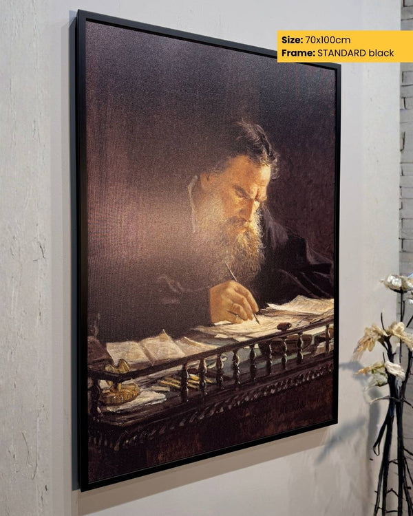 Framed artwork of a man writing on a desk against a light gray wall.