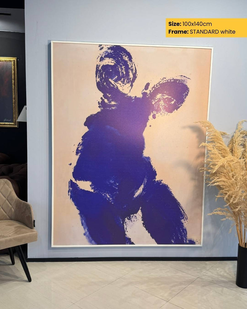 Abstract art print of a blue figure on a beige background, framed in white, in a room setting.