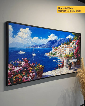 Framed artwork of a coastal scene with houses, boats, and flowers on a gray wall.