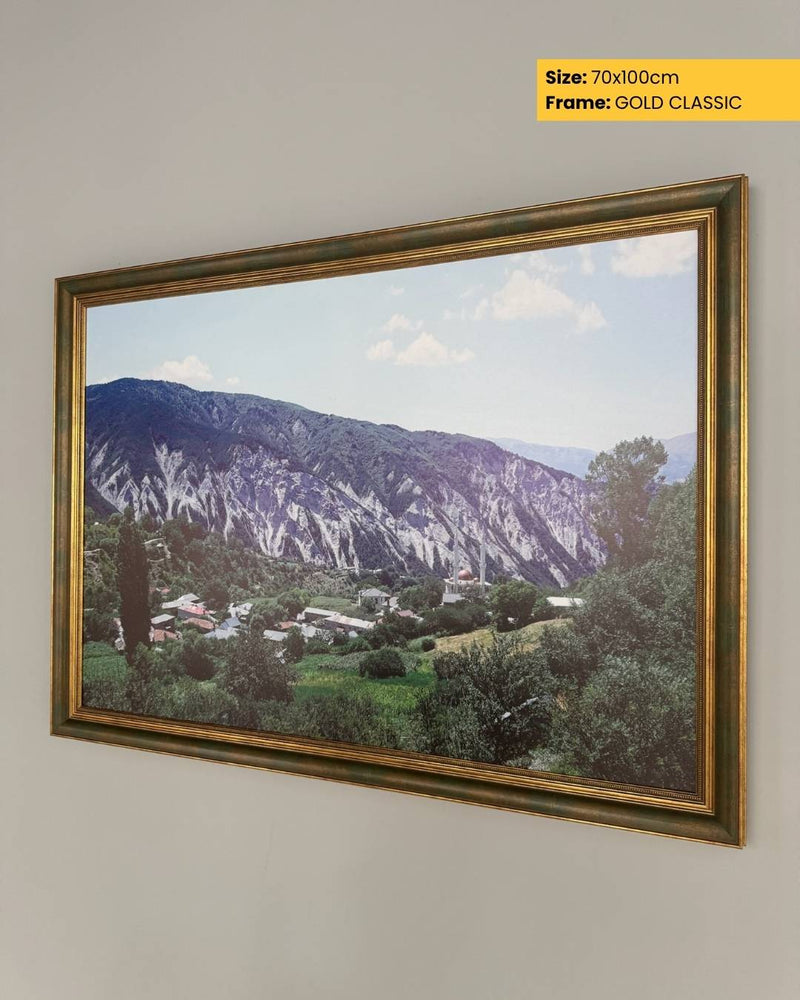 Framed landscape print of a mountainous area with a gold frame on a wall.