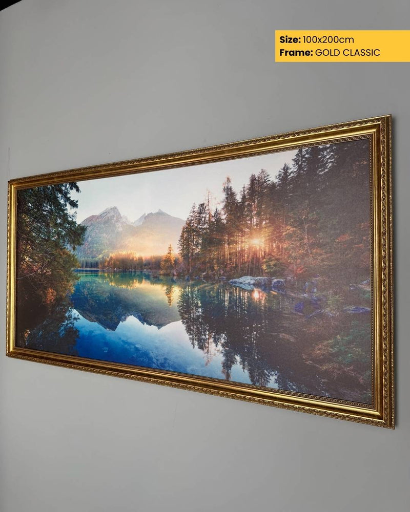 Framed landscape painting of a lake and mountains on a gray wall.