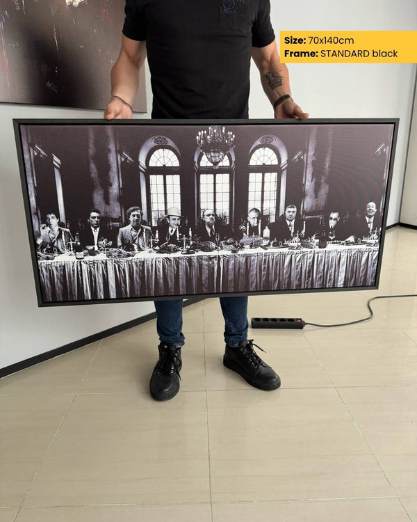 Person holding a large framed picture of a formal event with multiple people sitting at a table.
