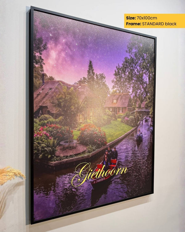 Framed artwork of a scenic view with a canal and houses, labeled 'Gieboldeham', on a white wall.
