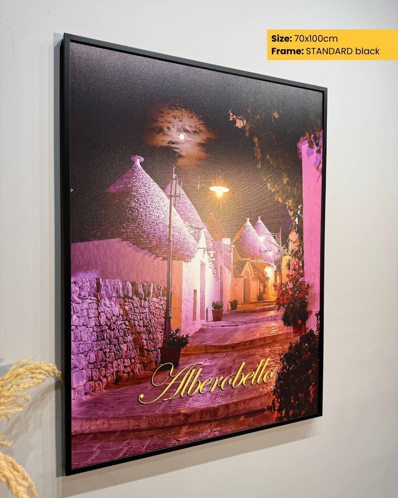 Framed artwork of a village scene with 'Alberobello' text, on a white wall.