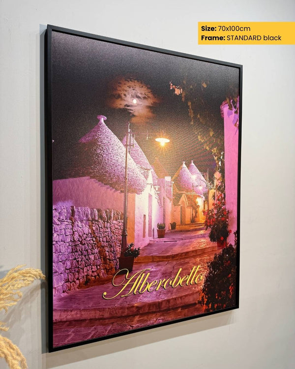 Framed artwork of a village scene with 'Alberobello' text, on a white wall.