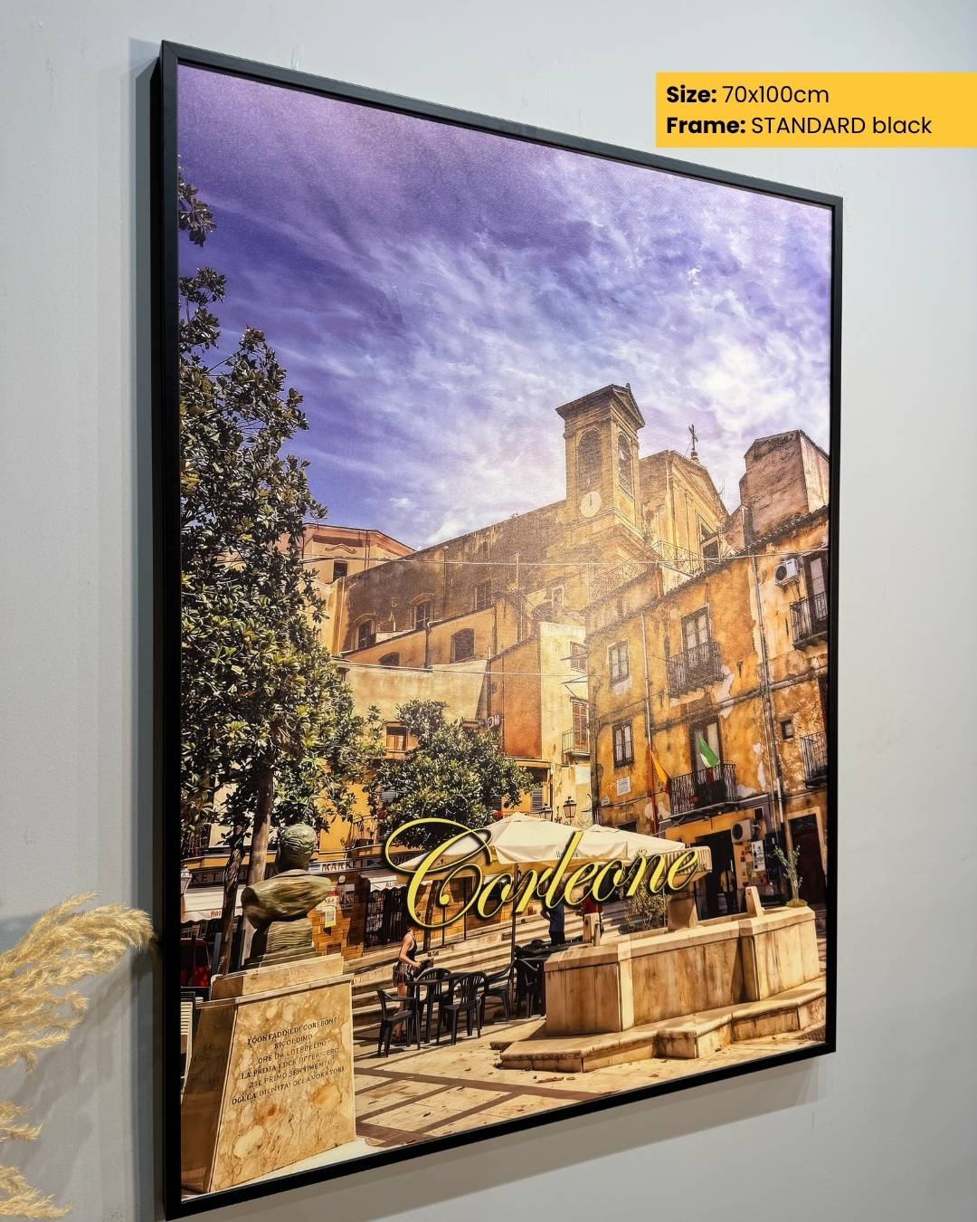 Framed artwork of a scenic street with 'Café' sign on a white wall.