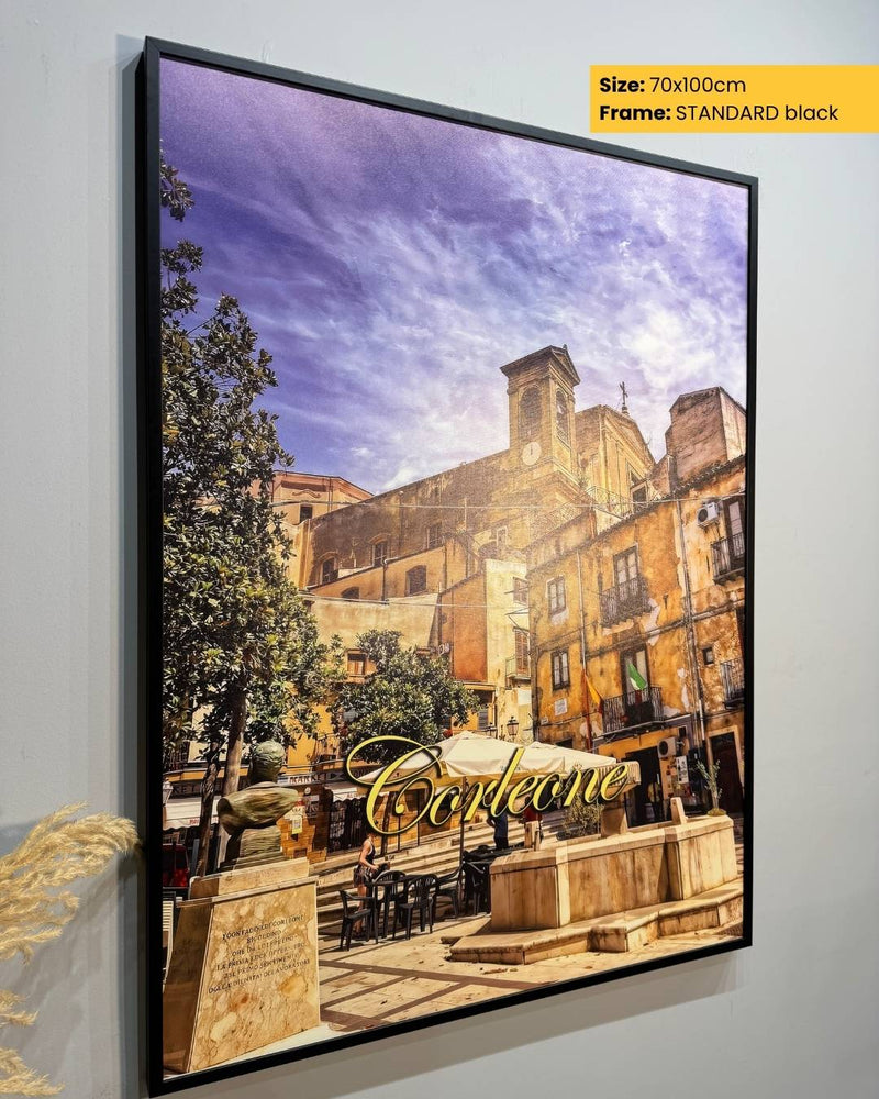 Framed artwork of a scenic street with 'Café' sign on a white wall.