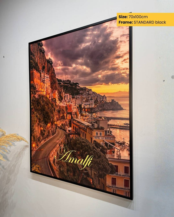 Framed artwork of a coastal town with 'Amalfi' text, displayed on a white wall.
