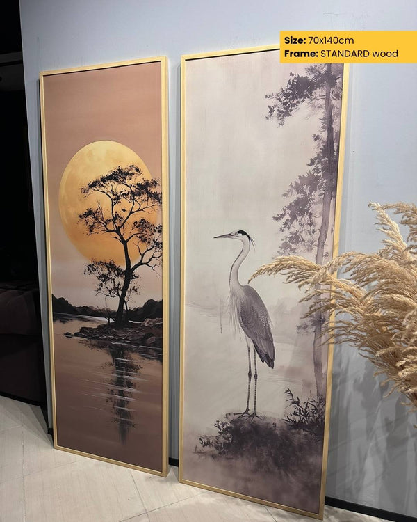 Two framed artworks with a landscape scene and a heron on a pebble, displayed against a light gray wall.