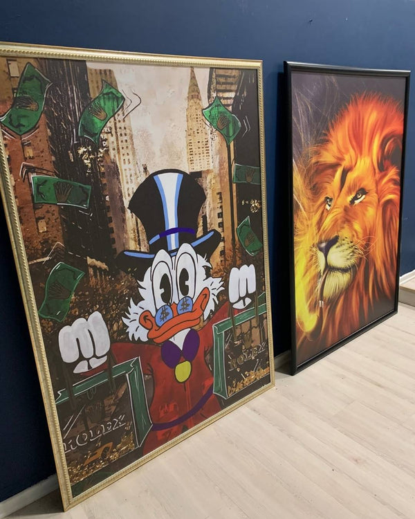 Two framed artworks side by side on a blue wall; one features a cartoon character and the other a lion's face.