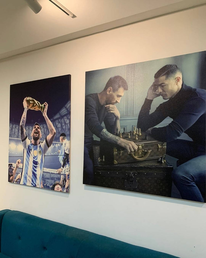 Two large wall art prints of a soccer player and two men playing chess on a white wall.