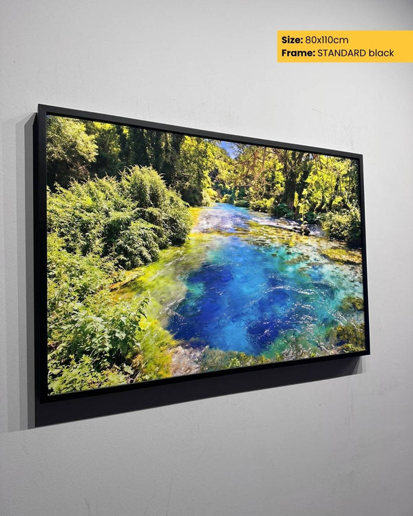 Framed artwork of a natural landscape with a river and trees on a gray wall.