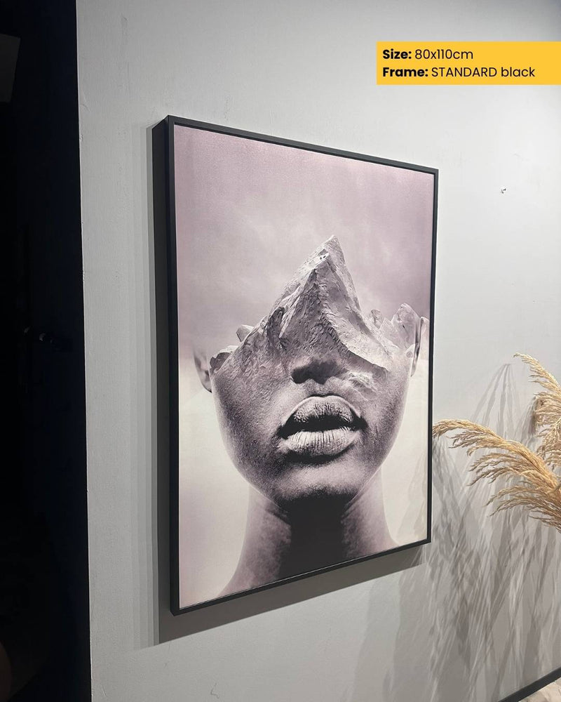 Framed black and white art print of a face on a wall.