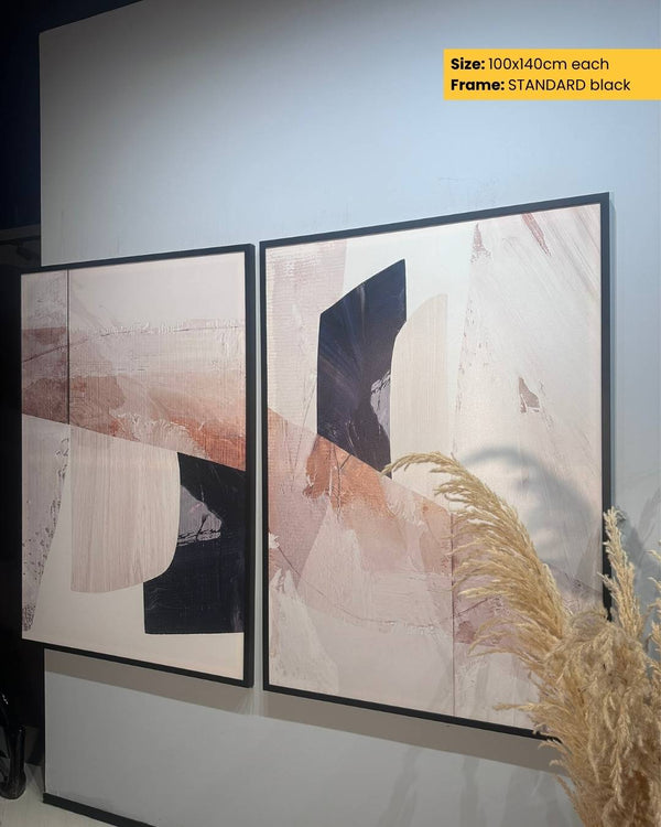 Two abstract art pieces in black frames on a wall with pampas grass.