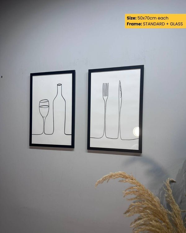 Two framed line art prints of a bottle, glass, fork, and knife on a wall.