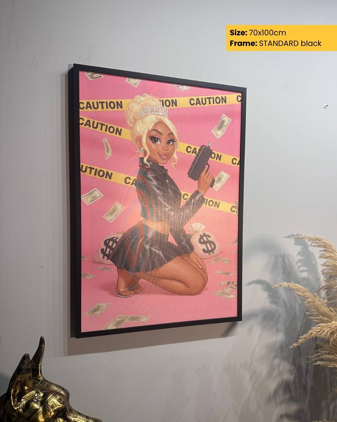 Framed artwork of a stylized character on a pink background with 'CAUTION' tape, held against a gray wall.