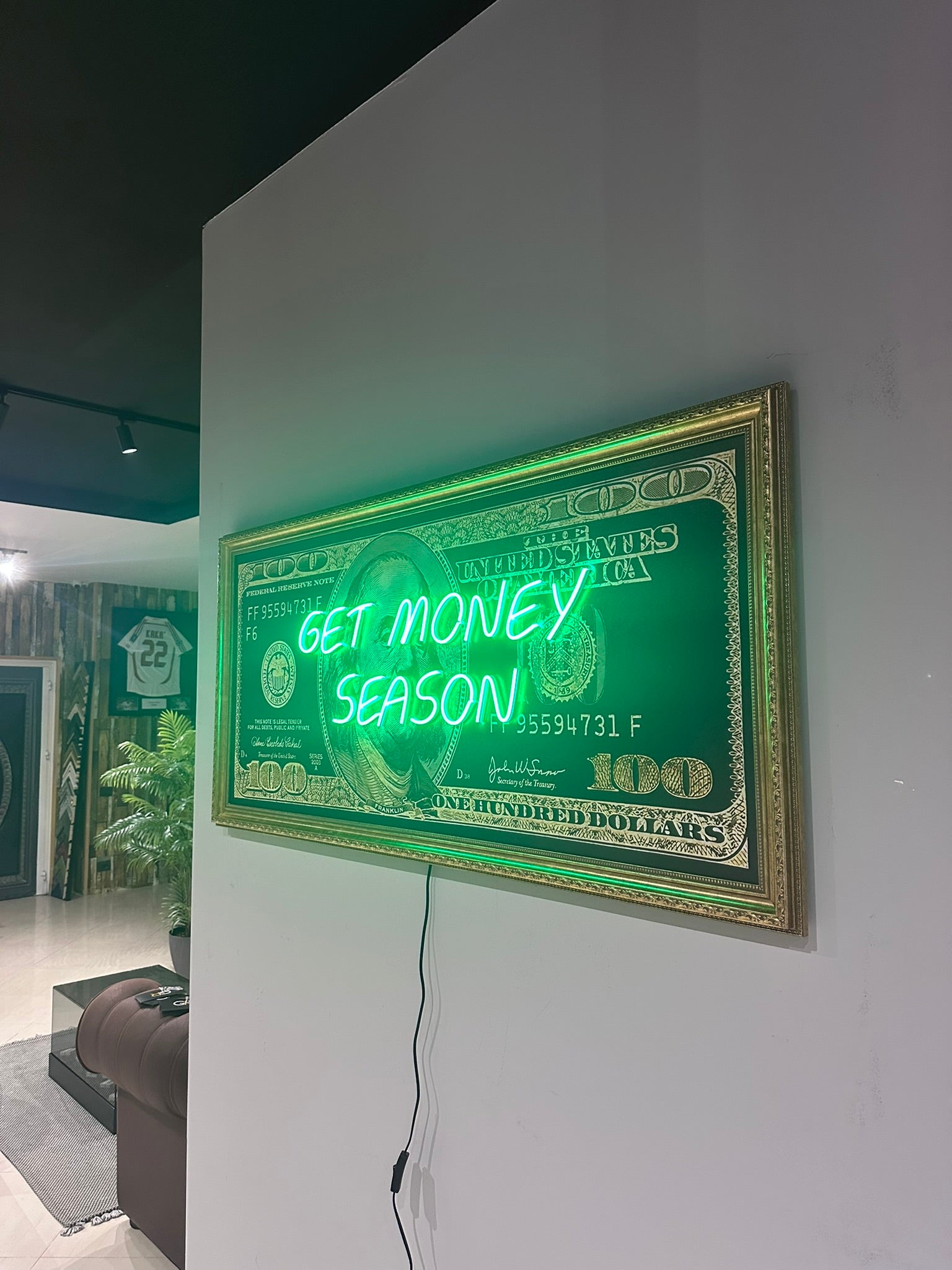 Neon sign with dollar bill design and 'Get Money Season' text on a wall.