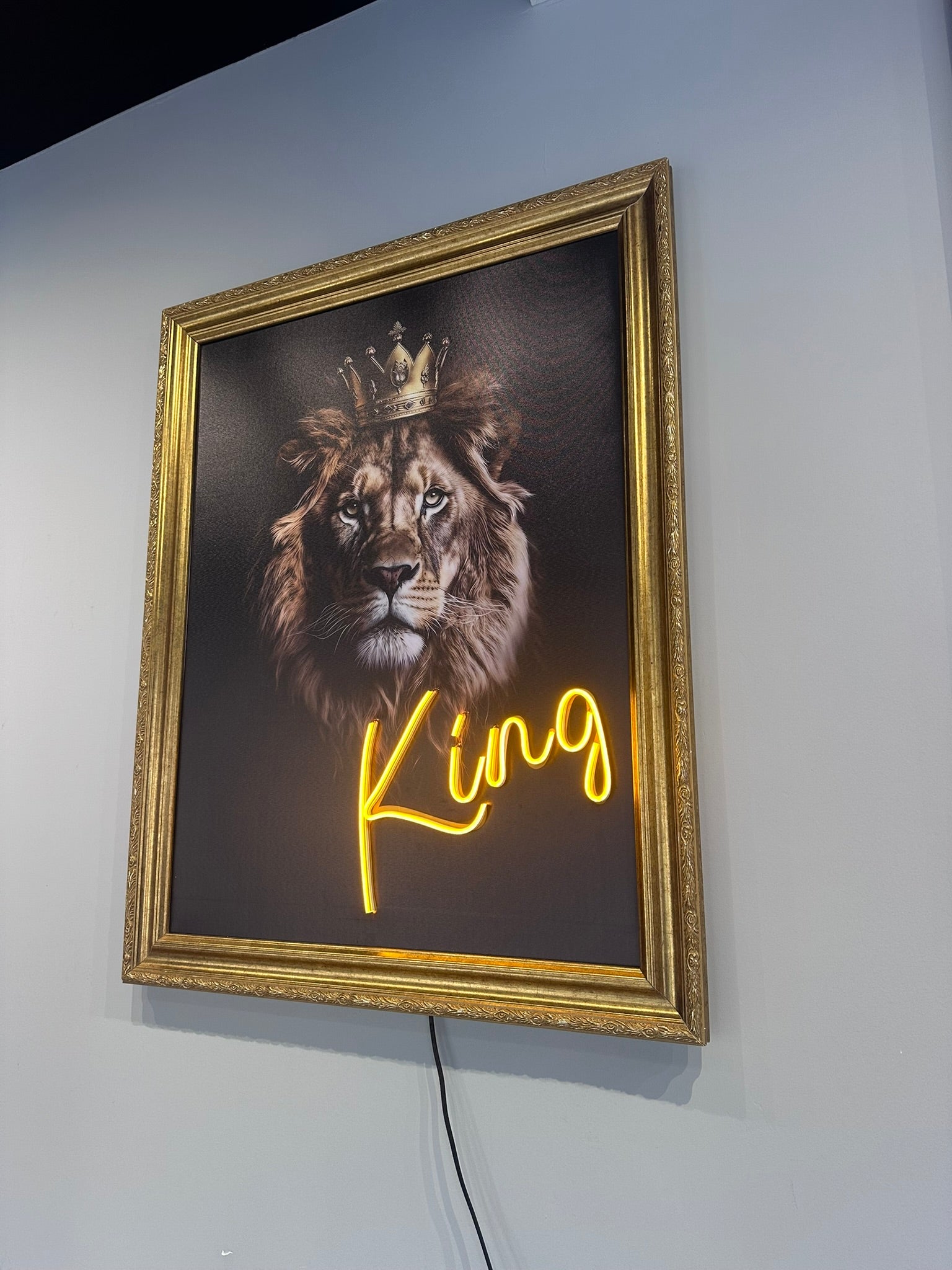 Neon sign with a lion's head and 'King' text in a gold frame on a white wall.