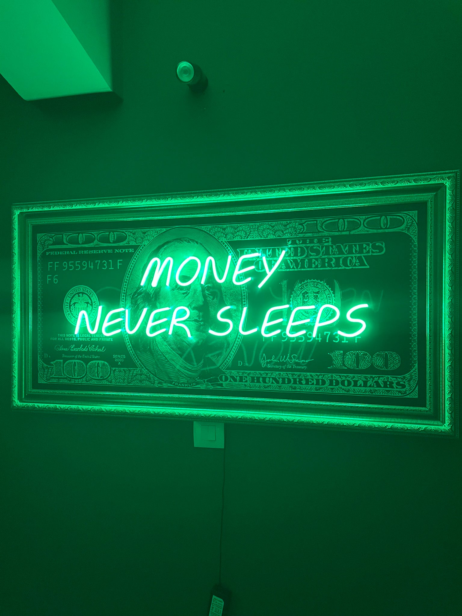 Neon sign with 'Money Never Sleeps' text on a green background