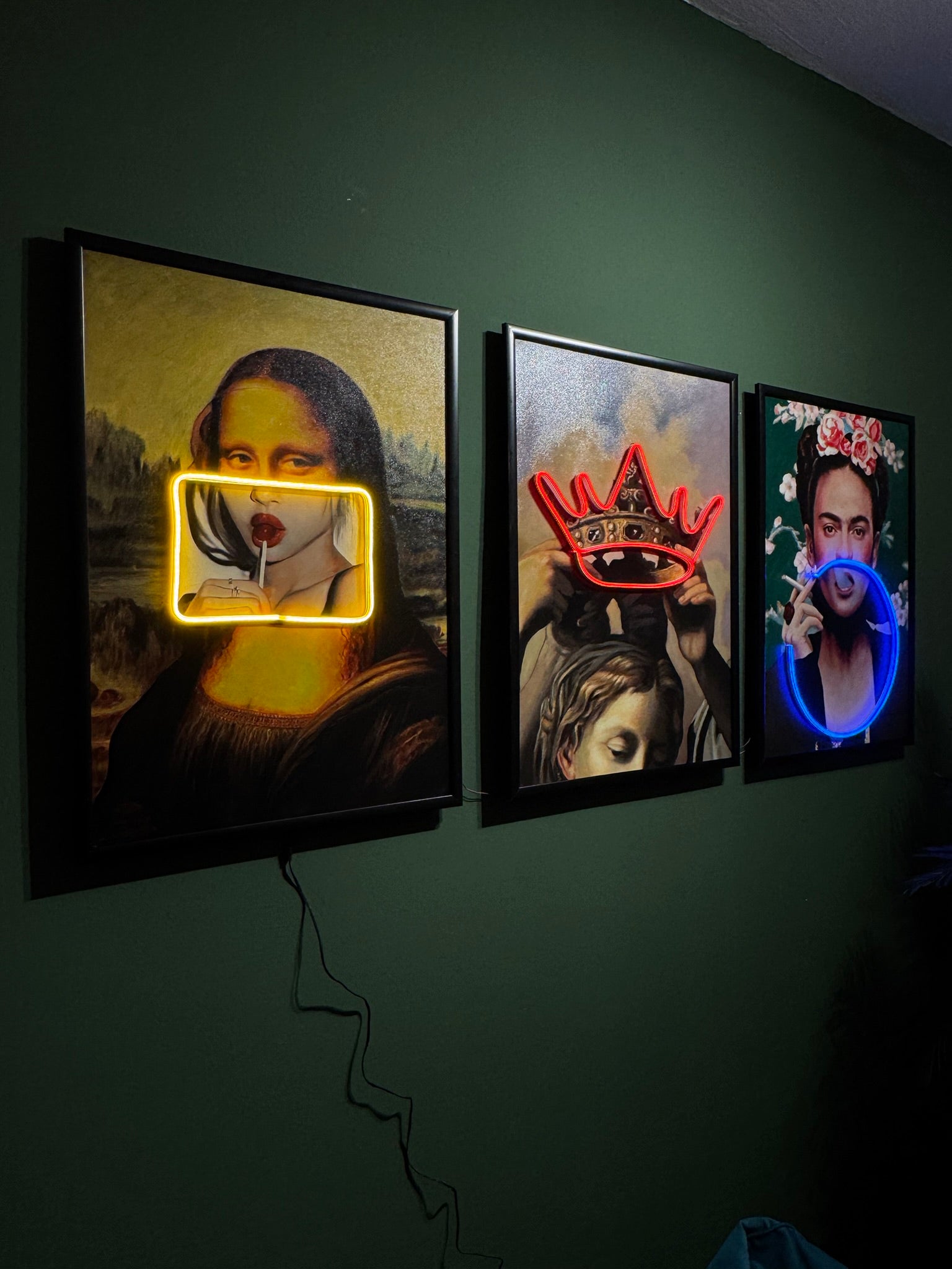 Three framed artworks with neon lights on a dark green wall