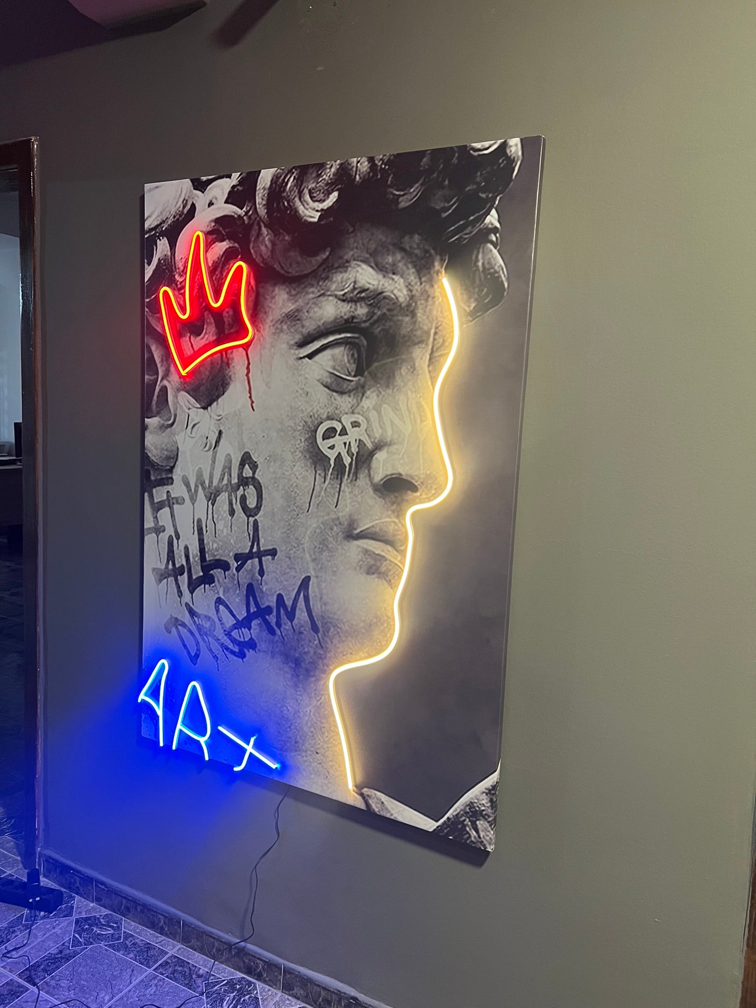 Neon art piece of a face with graffiti text on a wall.