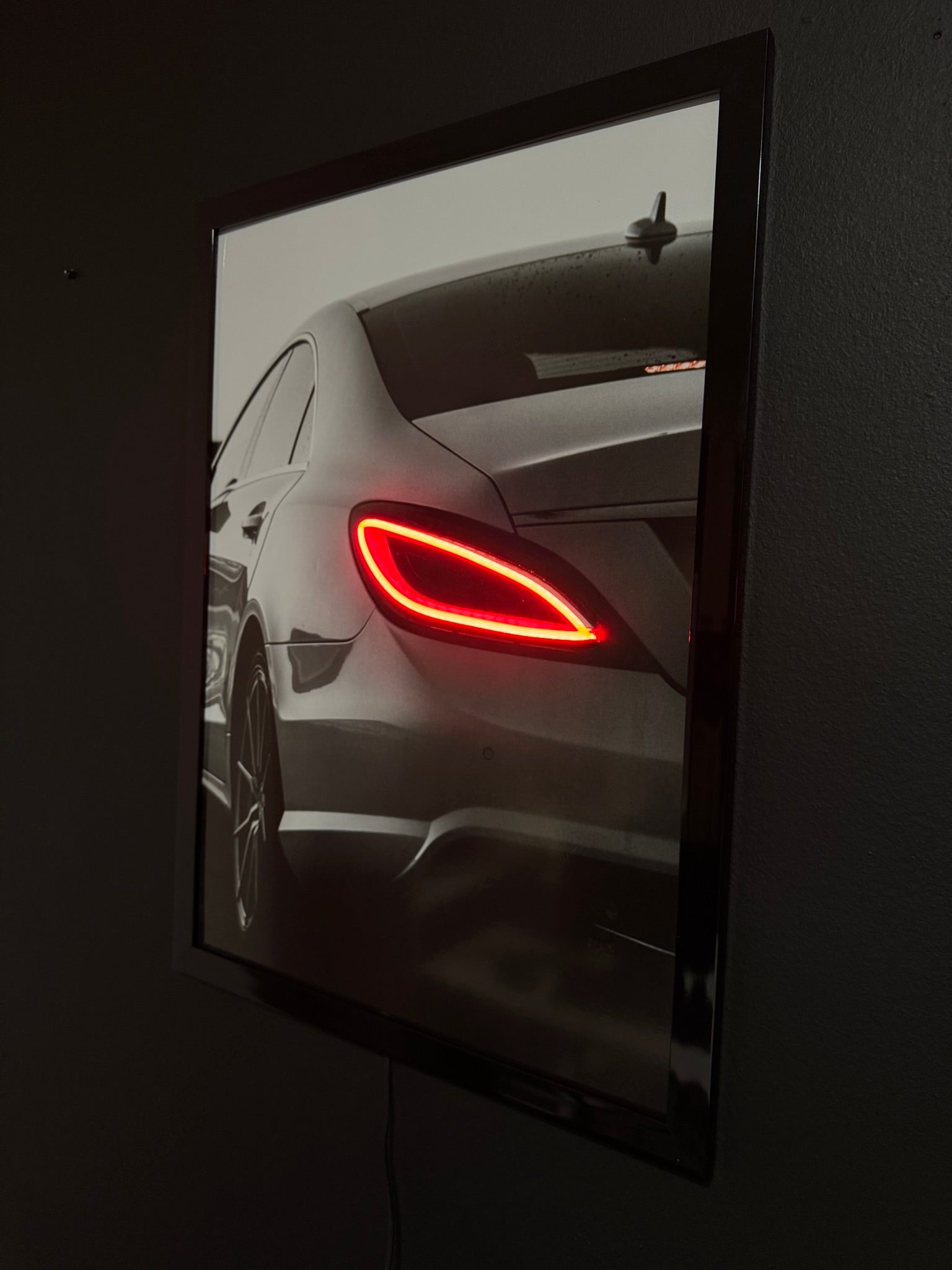 Car's red taillight reflected in a black-framed mirror on a dark background