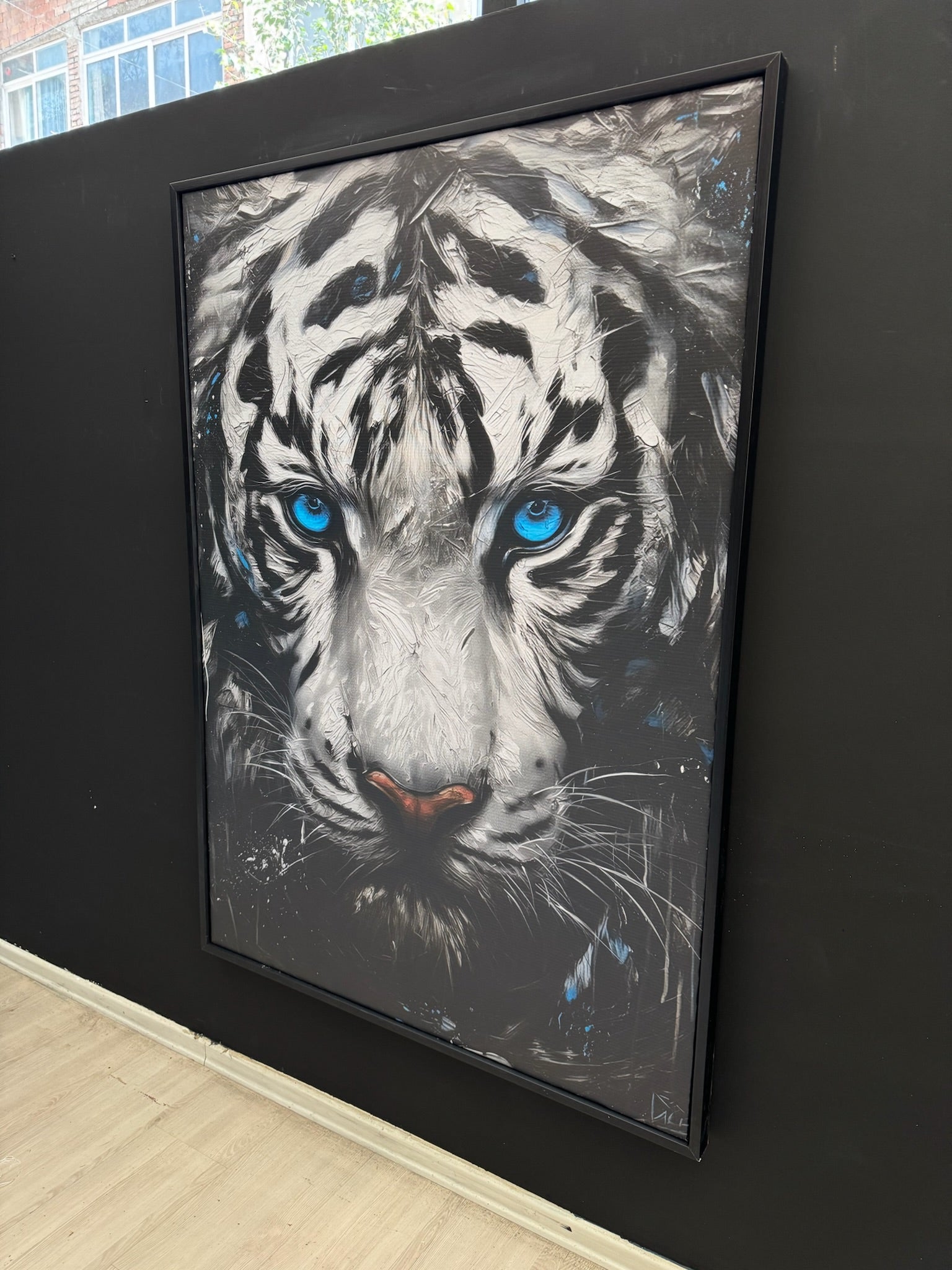 Framed painting of a tiger with blue eyes on a black wall.