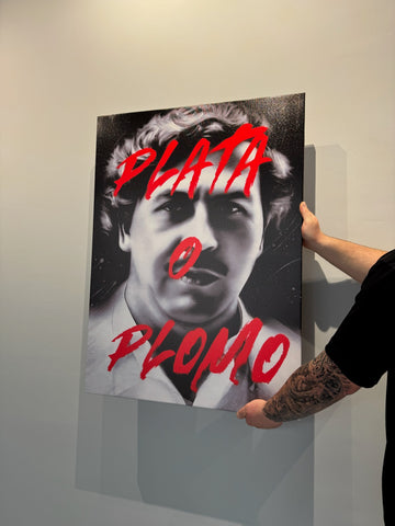 Person holding a poster with a black and white portrait and red text on a light gray wall.