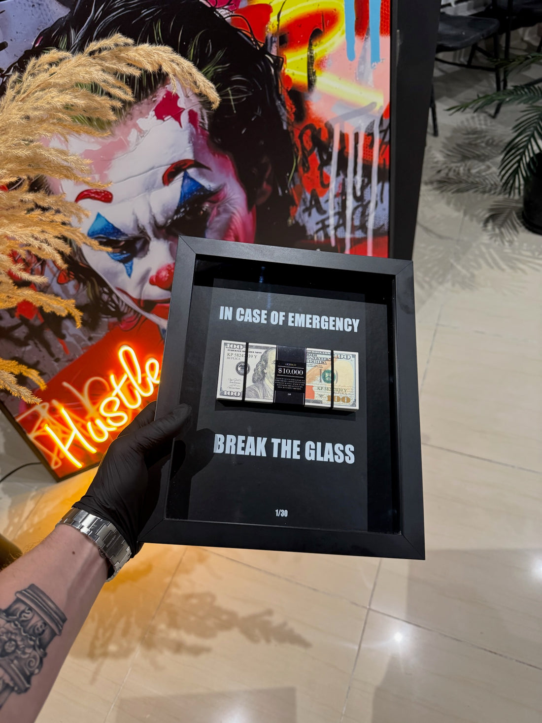 Framed artwork with text 'In case of emergency, break the glass' held by a person.