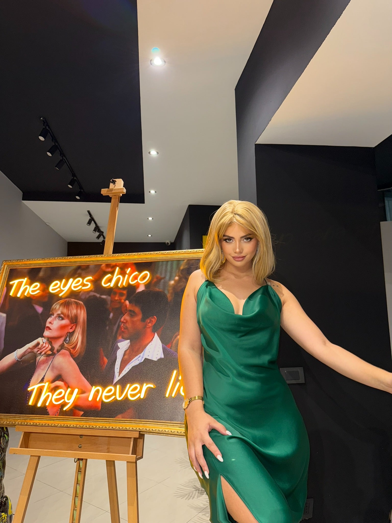 Woman in a green dress standing next to a painting with text in an indoor setting