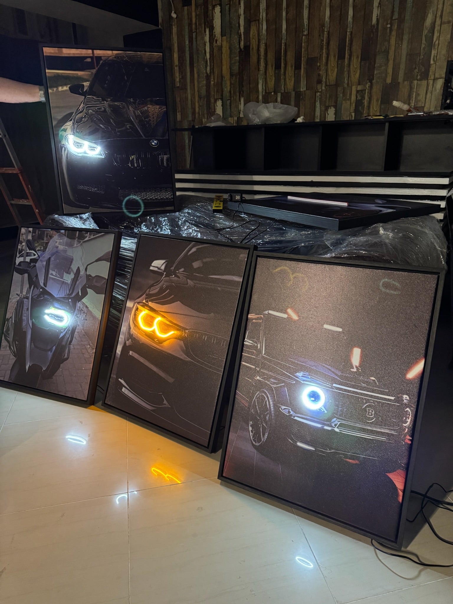 Multiple computer monitors displaying different car models with illuminated headlights on a tiled floor.