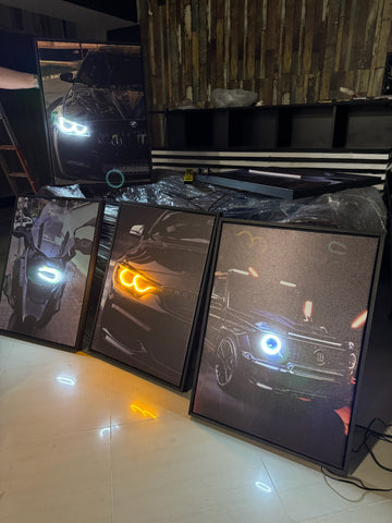 Multiple computer monitors displaying different car models with illuminated headlights on a tiled floor.
