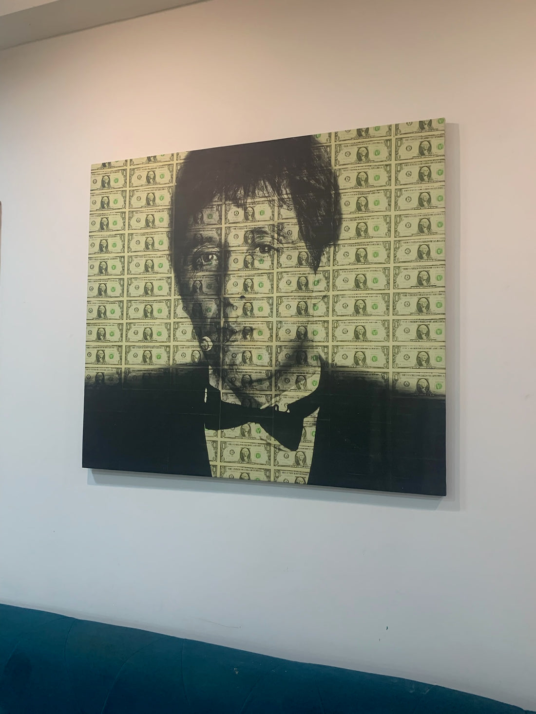 Framed artwork of a portrait with dollar bill pattern on a wall.