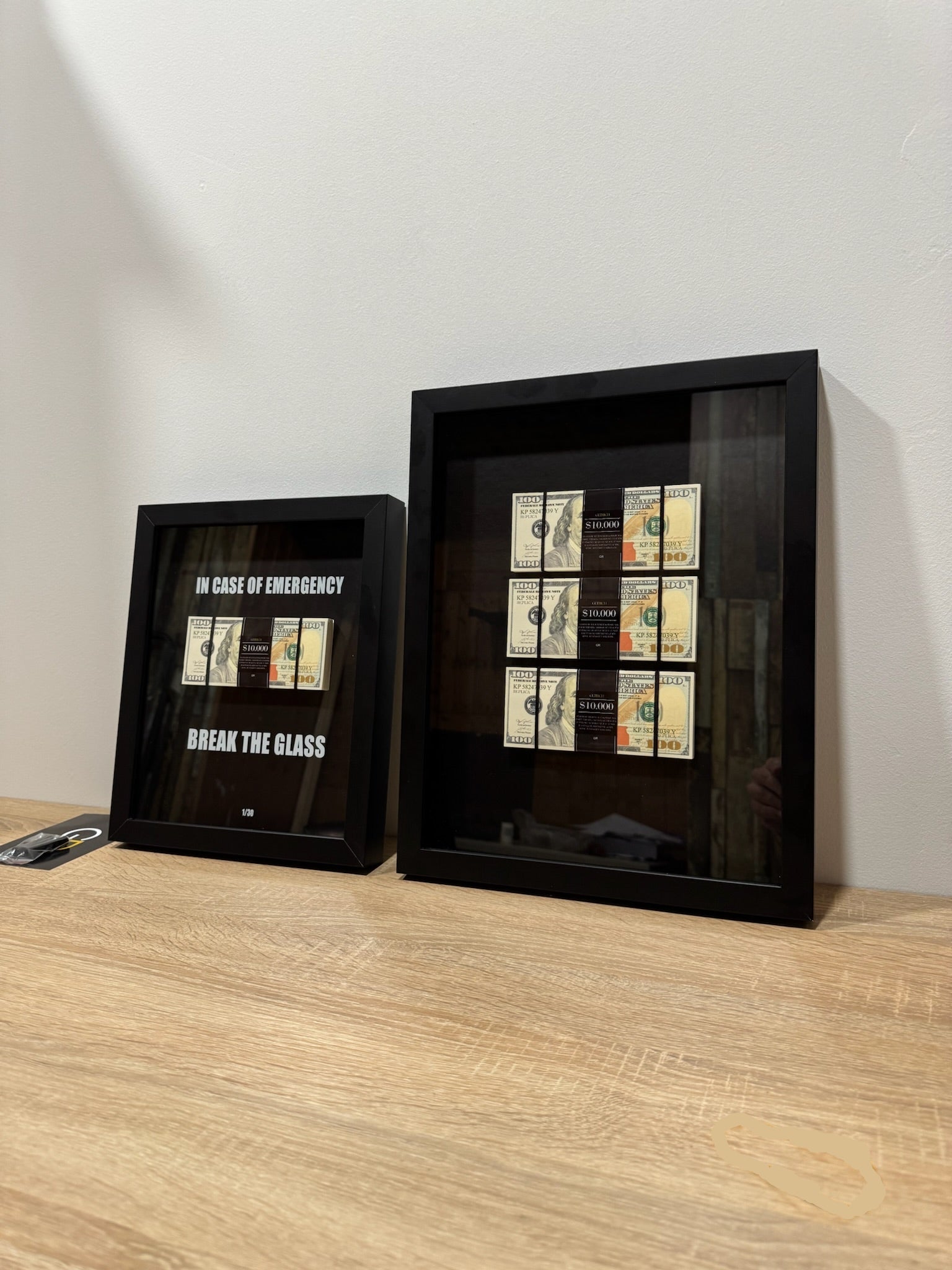 Two black framed collectible items on a wooden surface with a white wall background.