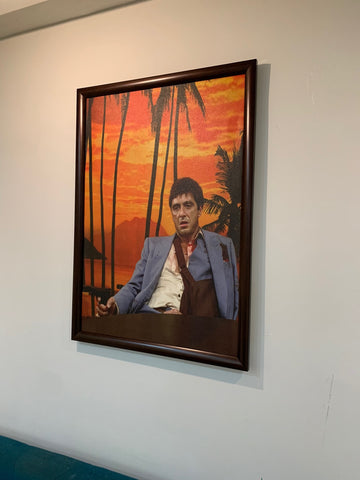 Framed artwork of a man sitting in front of a sunset with palm trees