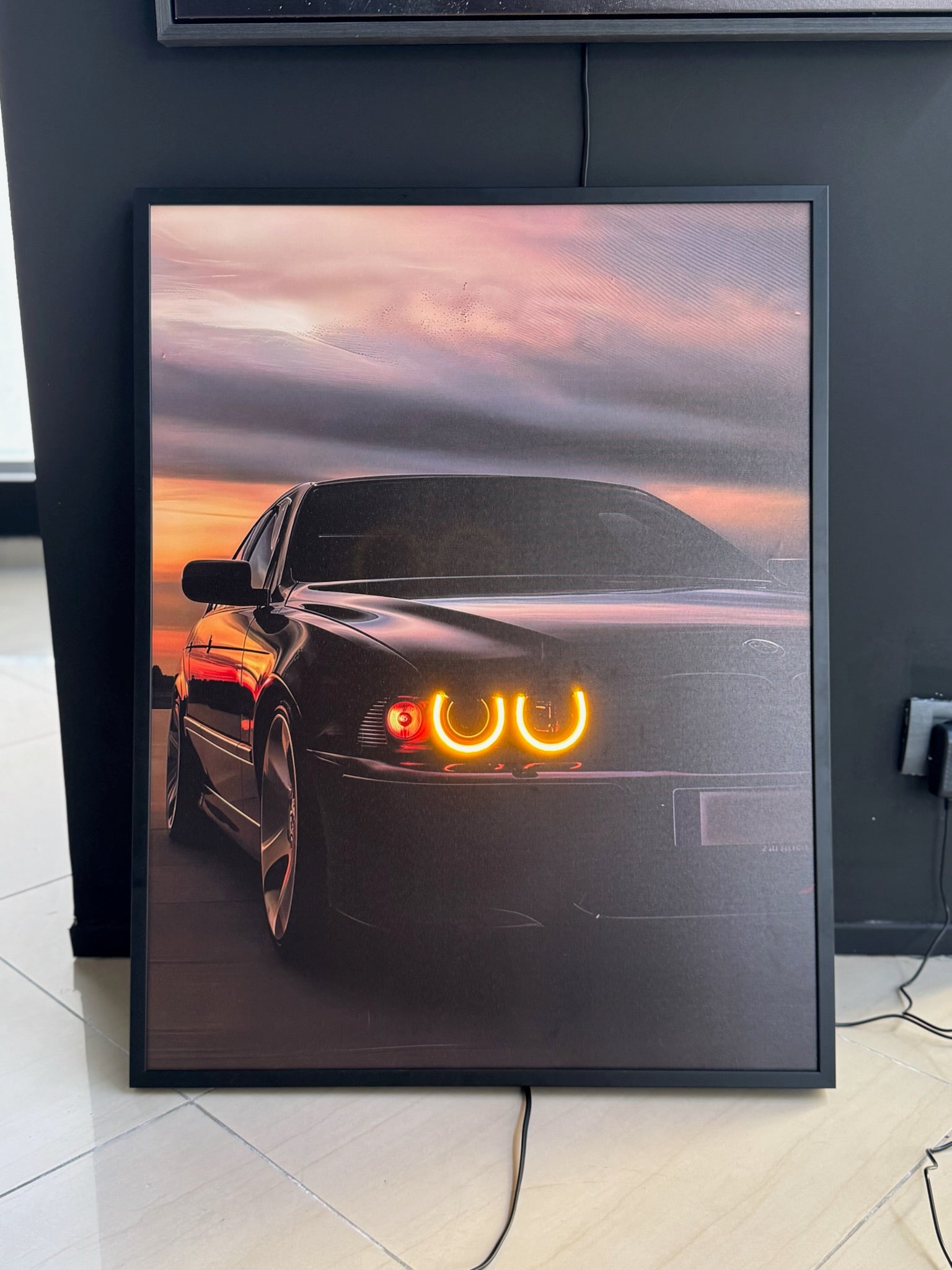 Framed artwork of a car with glowing headlights against a sunset sky.