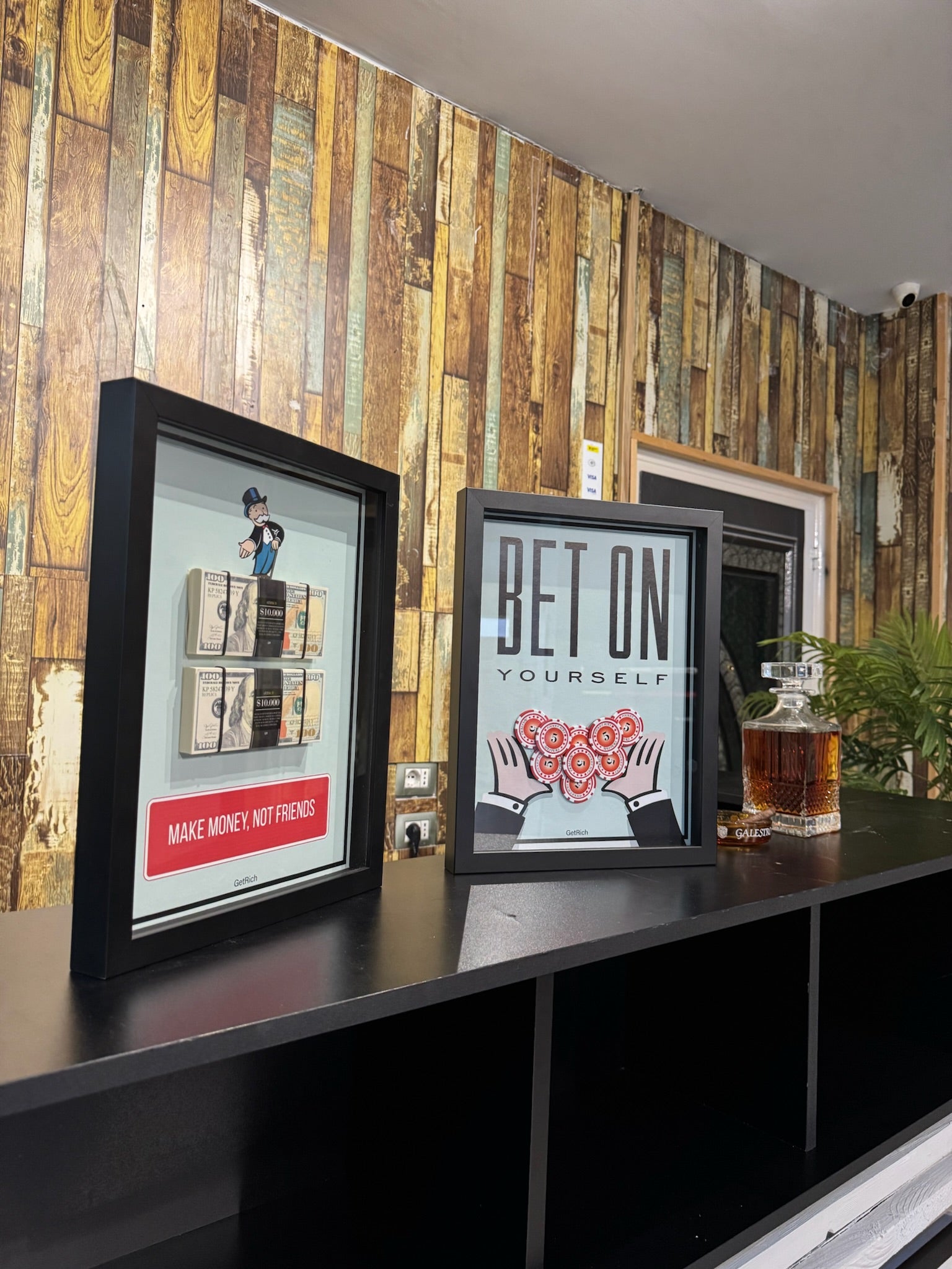 Two framed pictures on a shelf against a wooden paneled wall.