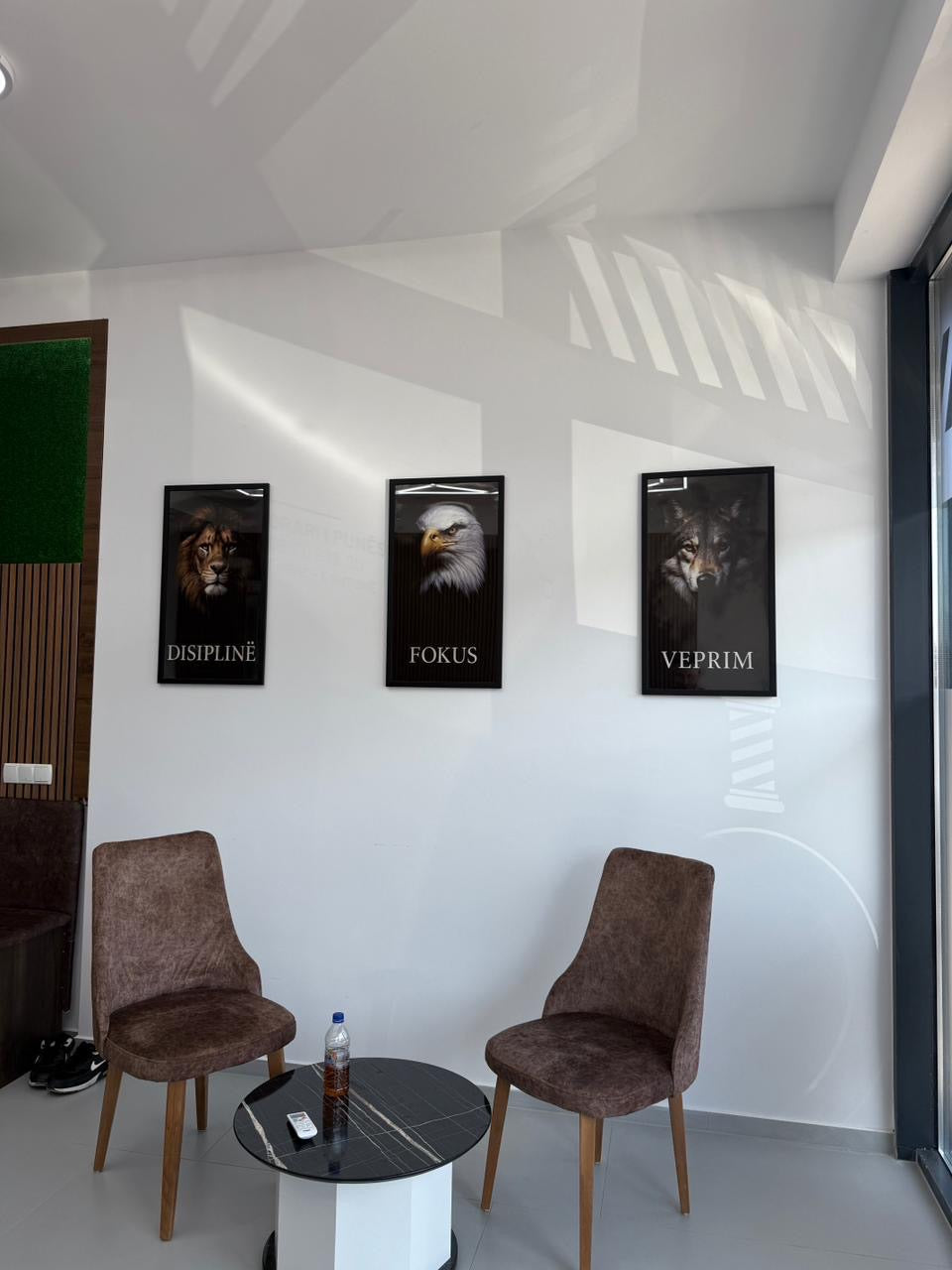 Modern interior with three framed posters on a white wall, two brown chairs, and a small round table.