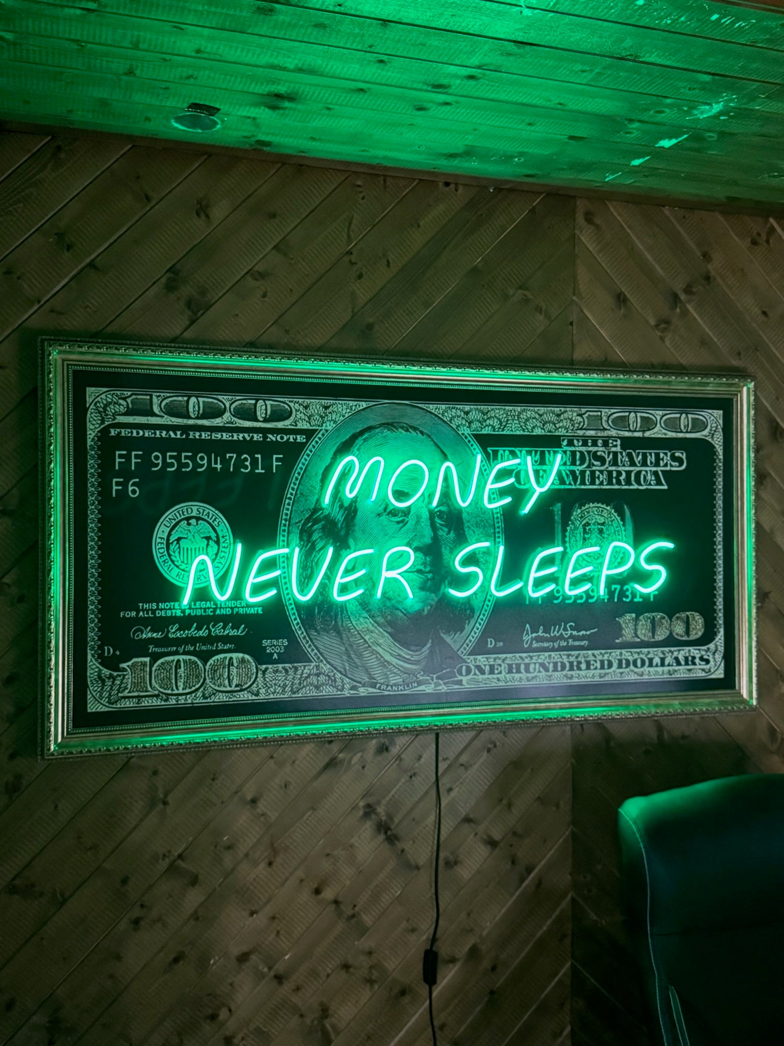 Neon sign of a dollar bill with 'Money Never Sleeps' text on a wooden wall.